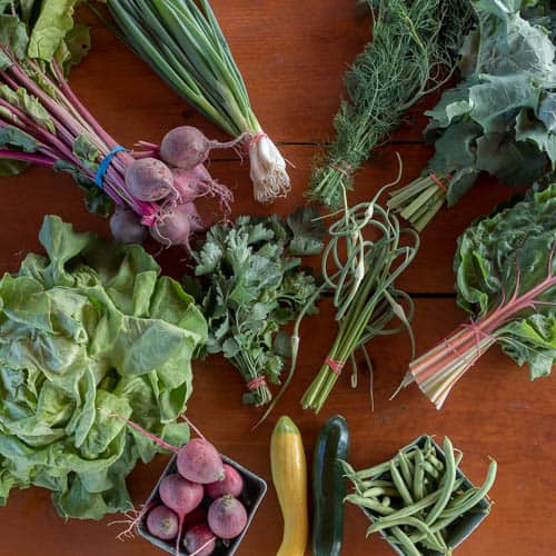 variety of local organic vegetables laid out on a burgundy coloured wooden table