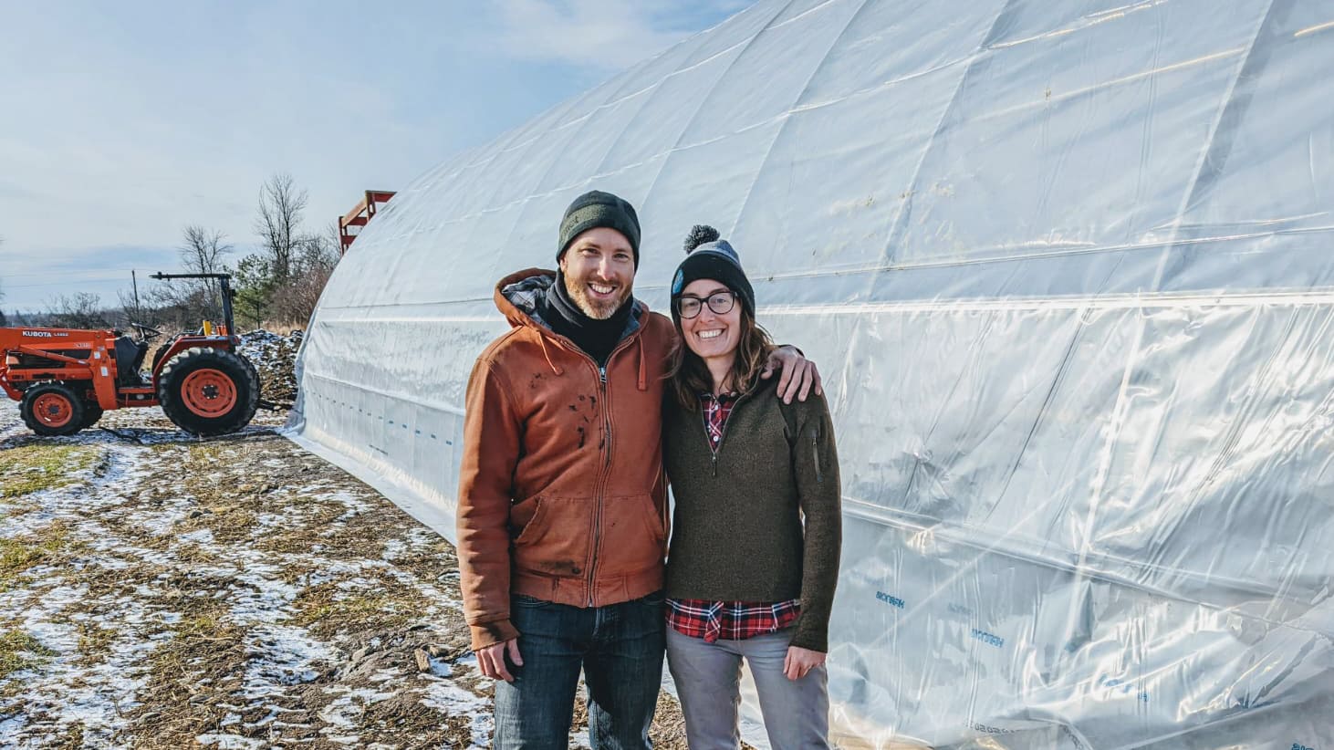 farmers kate and david stand in front of the greenhouse with big smiles