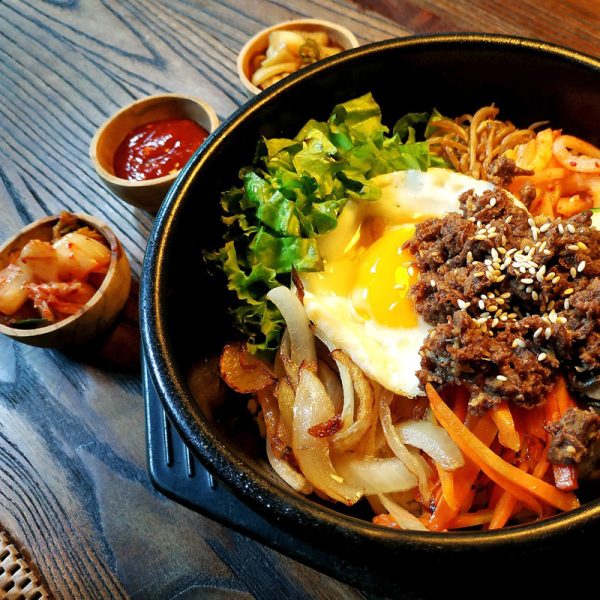 a bibimbap bowl with kimchi, chopped vegetables, marinated beef, and a fried egg