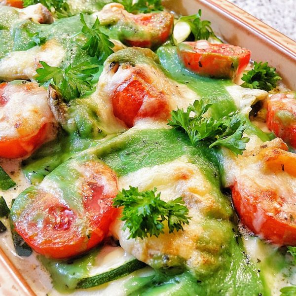 close up of a baked tomato, zucchini, and cheese dish topped with pesto and parsley