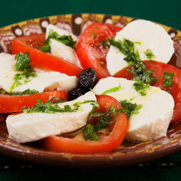 close up of a dish made up of fresh tomatoes, mozzarella, olives, and pesto