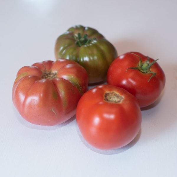 four whole organic tomatoes of mixed varieties on a white table