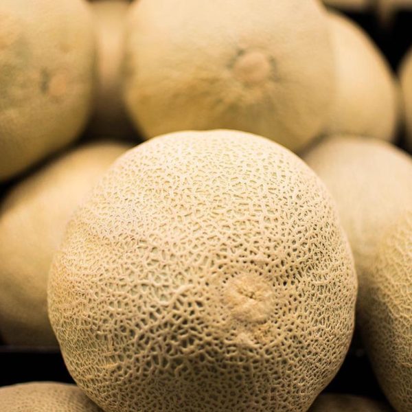 melons (cantaloupes) stacked in a pile with a closeup on the webbed texture of one melon