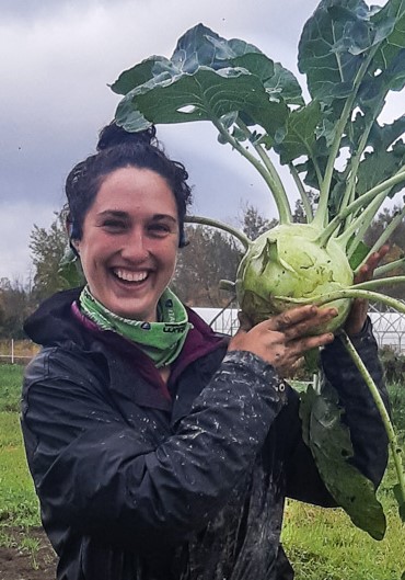 A young woman holds a giant kohlrabi that's the size of her head