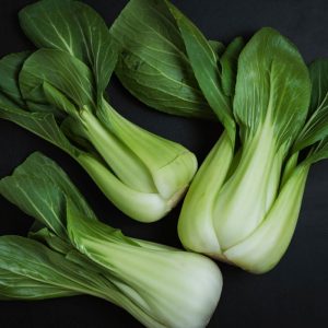 Three heads of organic shanghai bok choy on a black table.