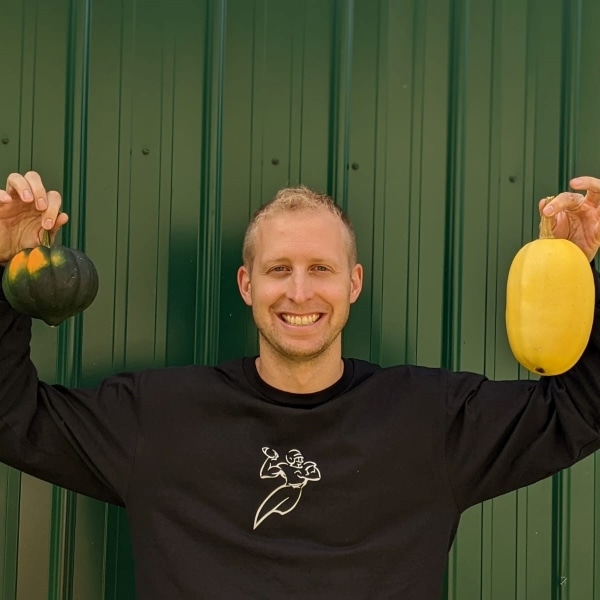 happy and smiling white man holds up two different types of winter squashes