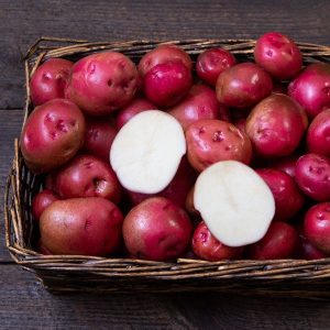 Organic red norland potatoes in a wicker basket with one potato sliced in half exposing white flesh